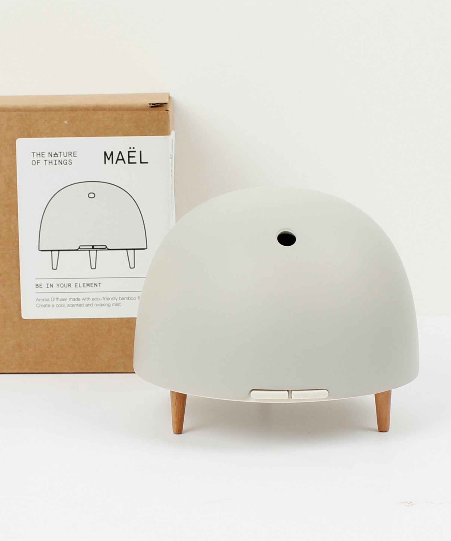 Maël Diffuser, a light grey dome plug-in essential oil diffuser with wooden feet, and cardoard packaging behind. 