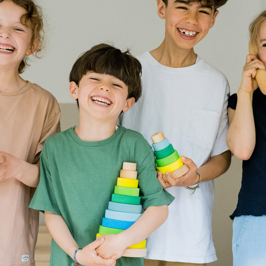 Grimm's Conical Stacking Tower - Neon Green - Four children are laughing and playing. Two of them are holding the Grimm's Conical Stacking Tower - Neon Green - Both sizes of the stacking tower are shown.