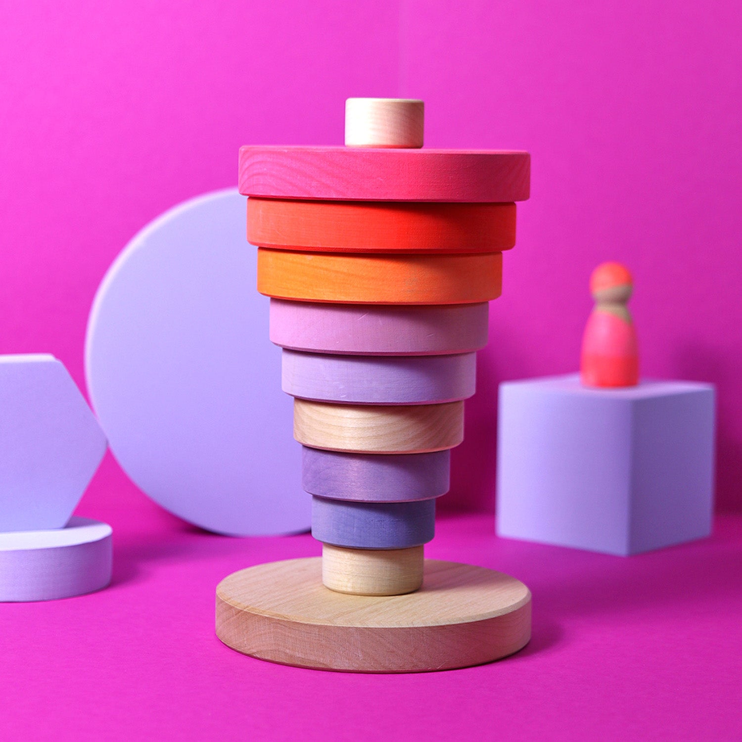 Grimm's Conical Stacking Tower - Neon Pink - On a plain blue background. The puzzle pieces are half on the stand and half off the stand.