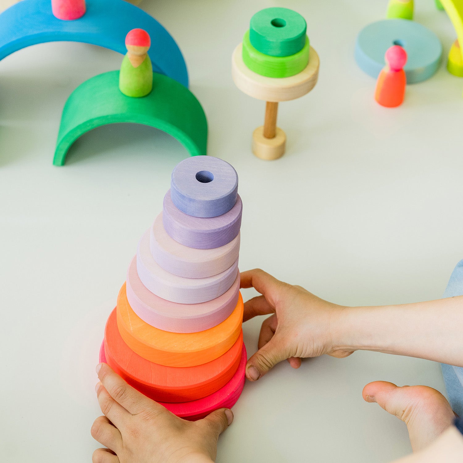 Grimm's Conical Stacking Tower - Neon Pink - In a home environment. Grimm's Neon Mix Friends are in the foreground.