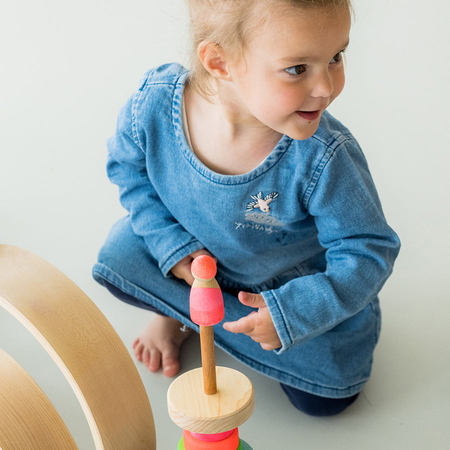 Grimm's Small Conical Stacking Tower - Neon Pink - On a plain blue background. Grimm's Neon Mix Friends are in front and on top of the Tower.