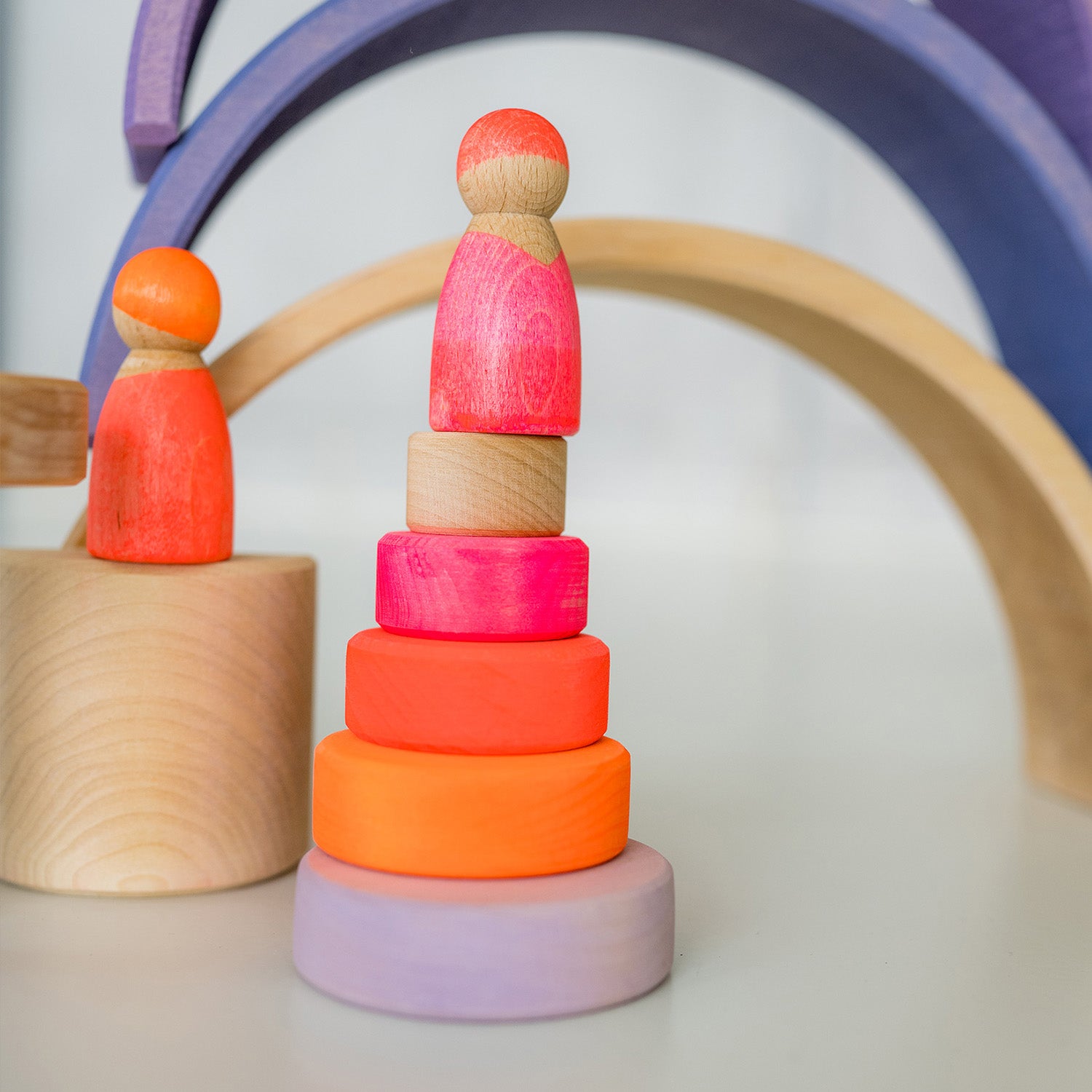 Grimm's Small Conical Stacking Tower - Neon Pink - On a plain blue background. Grimm's Neon Green Friends are in front and on top of the Tower. The puzzle has an alternative layout.