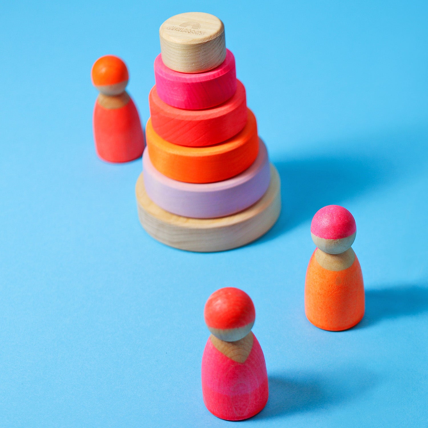 Grimm's Small Conical Stacking Tower - Neon Pink - On a plain blue background. Grimm's Neon Pink Friends are in front and to the side of the Tower. The tower is in separate pieces.