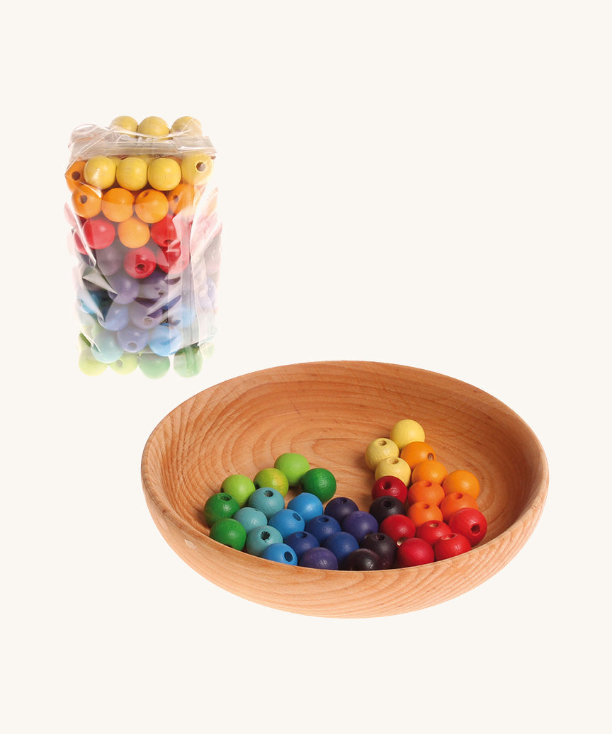 Rainbow coloured wooden Grimms beads in bag and in a wooden bowl on a cream background.