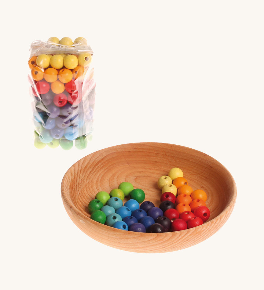 Rainbow coloured wooden Grimms beads in bag and in a wooden bowl on a cream background.