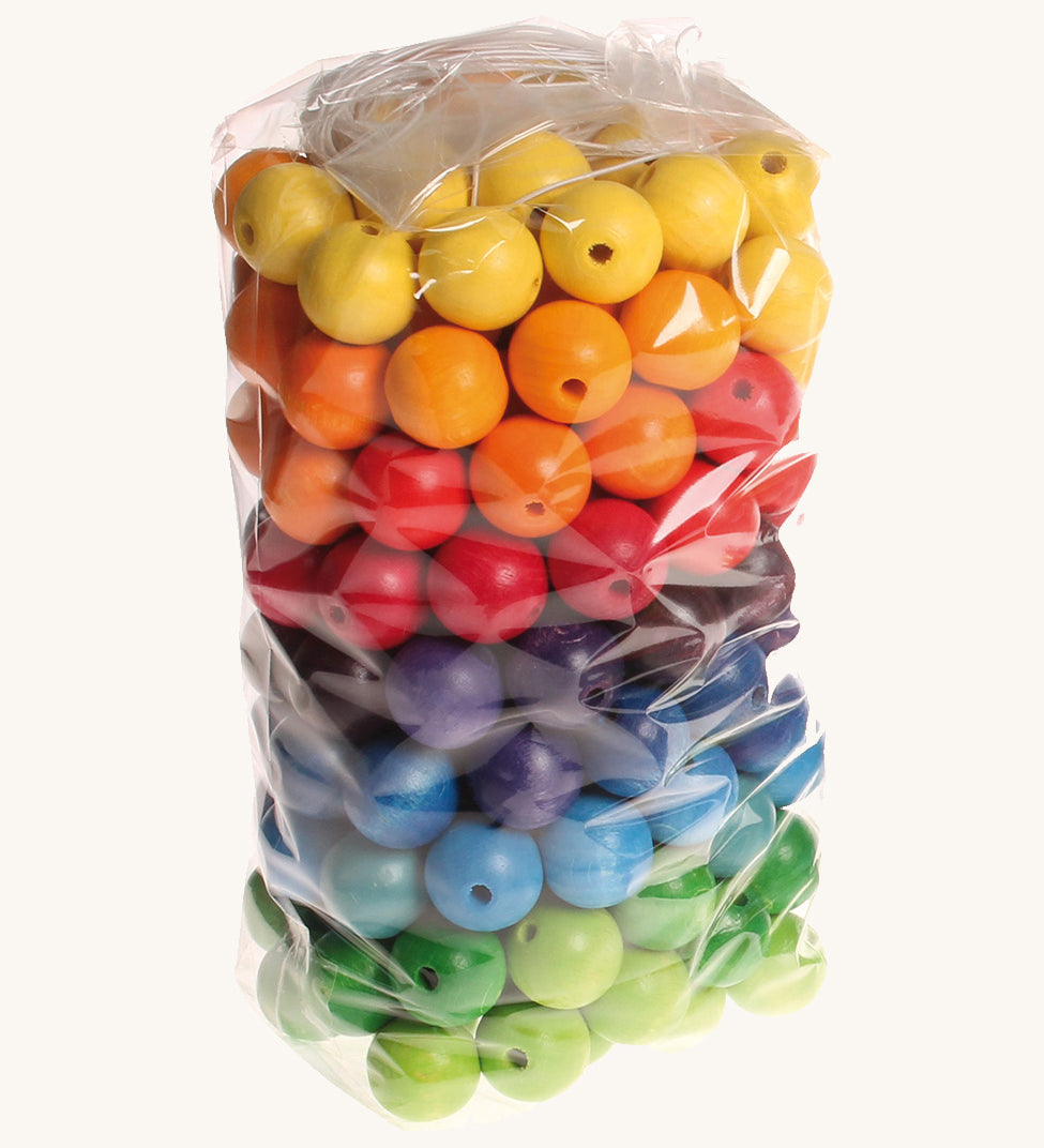 Rainbow coloured wooden Grimms beads in bag on a cream background.