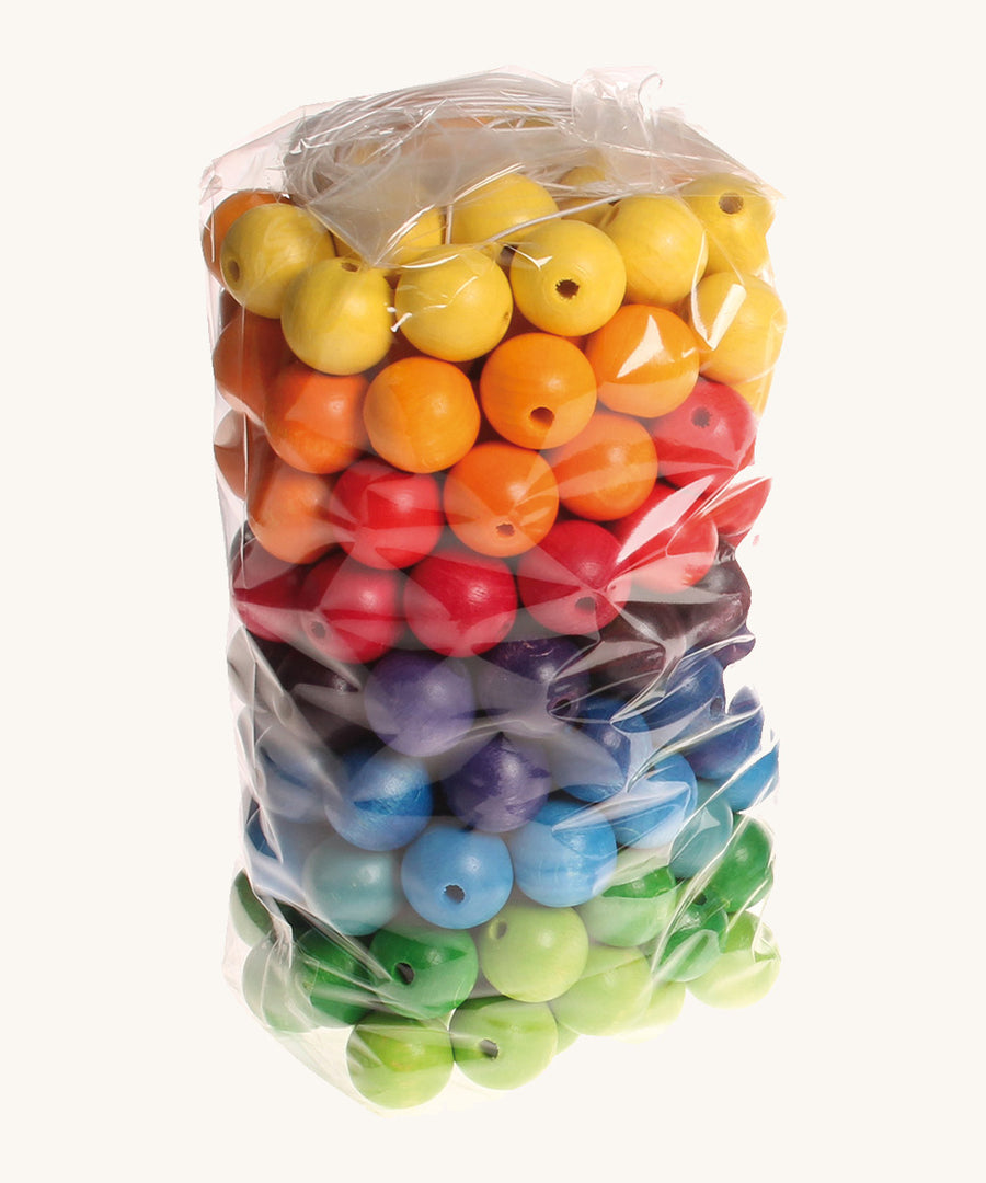 Rainbow coloured wooden Grimms beads in bag on a cream background.