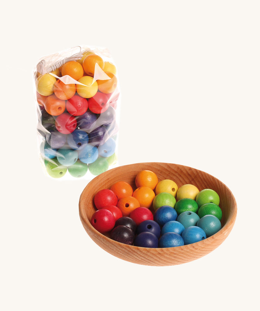 Rainbow coloured wooden Grimms beads in a wooden bowl and packaging on a cream background.