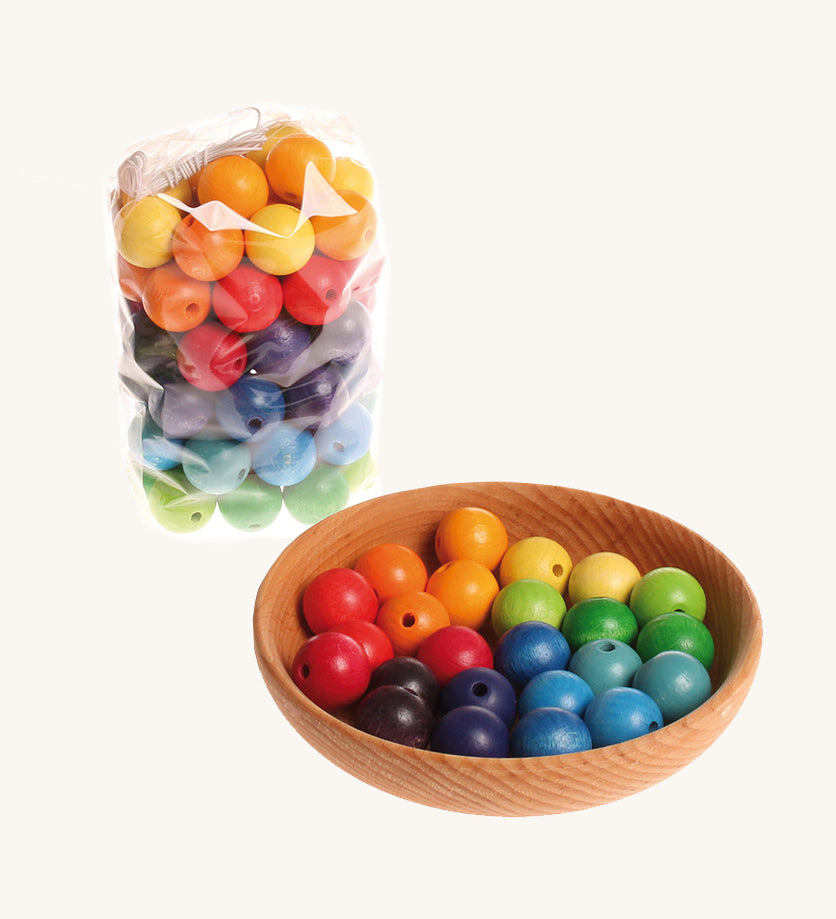 Rainbow coloured wooden Grimms beads in a wooden bowl and packaging on a cream background.