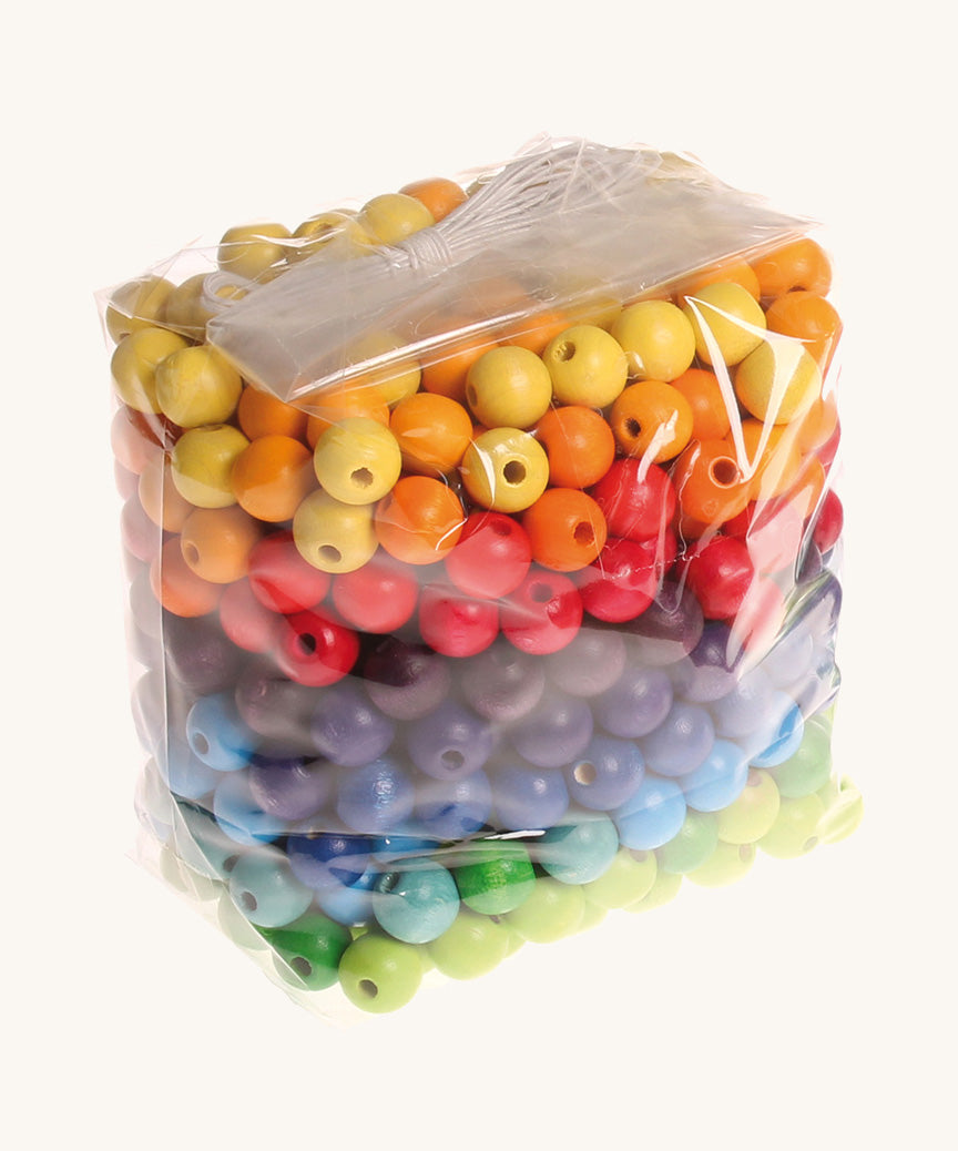 Rainbow coloured wooden Grimms beads in bag on a cream background.