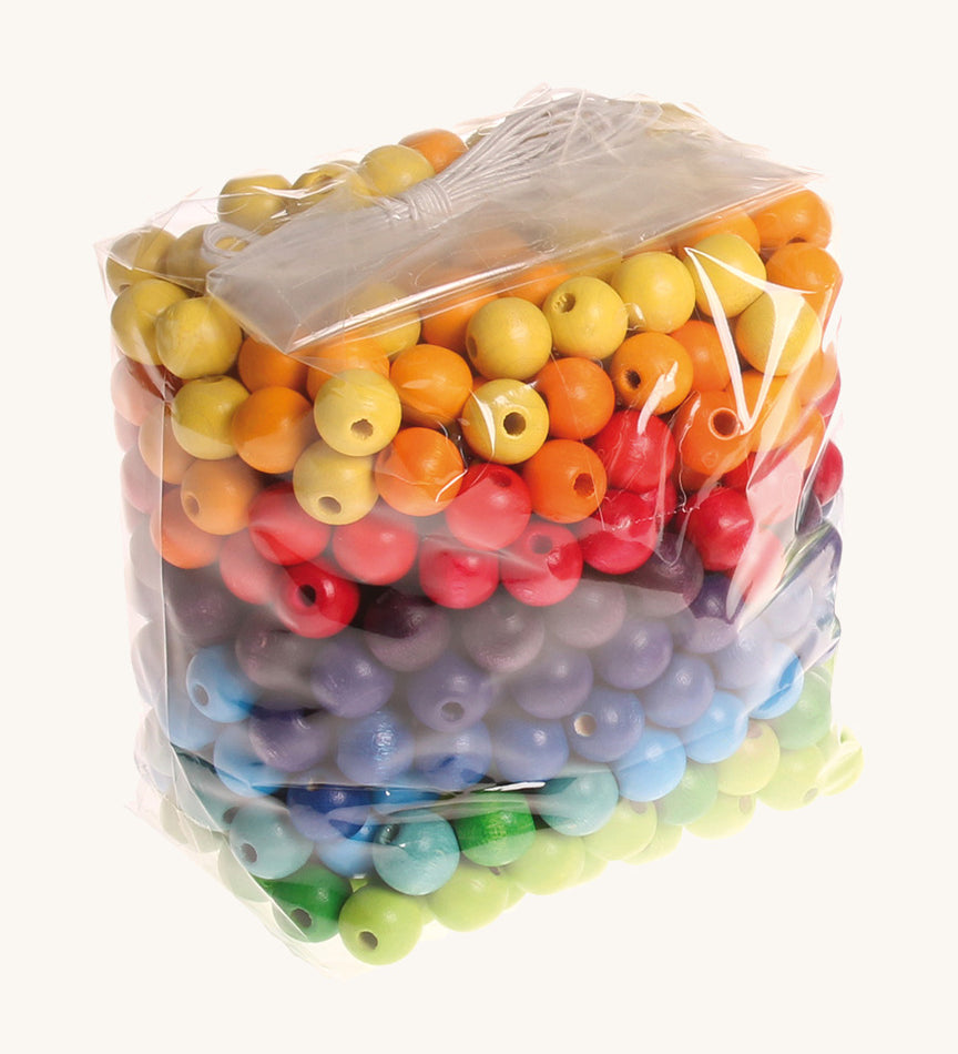 Rainbow coloured wooden Grimms beads in bag on a cream background.