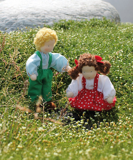 Grimm's Brown Haired Girl Doll - Lana is sat on a flowery patch of grass with another Grimm's Waldorf Doll - Linde, handmade, fabric doll next to it