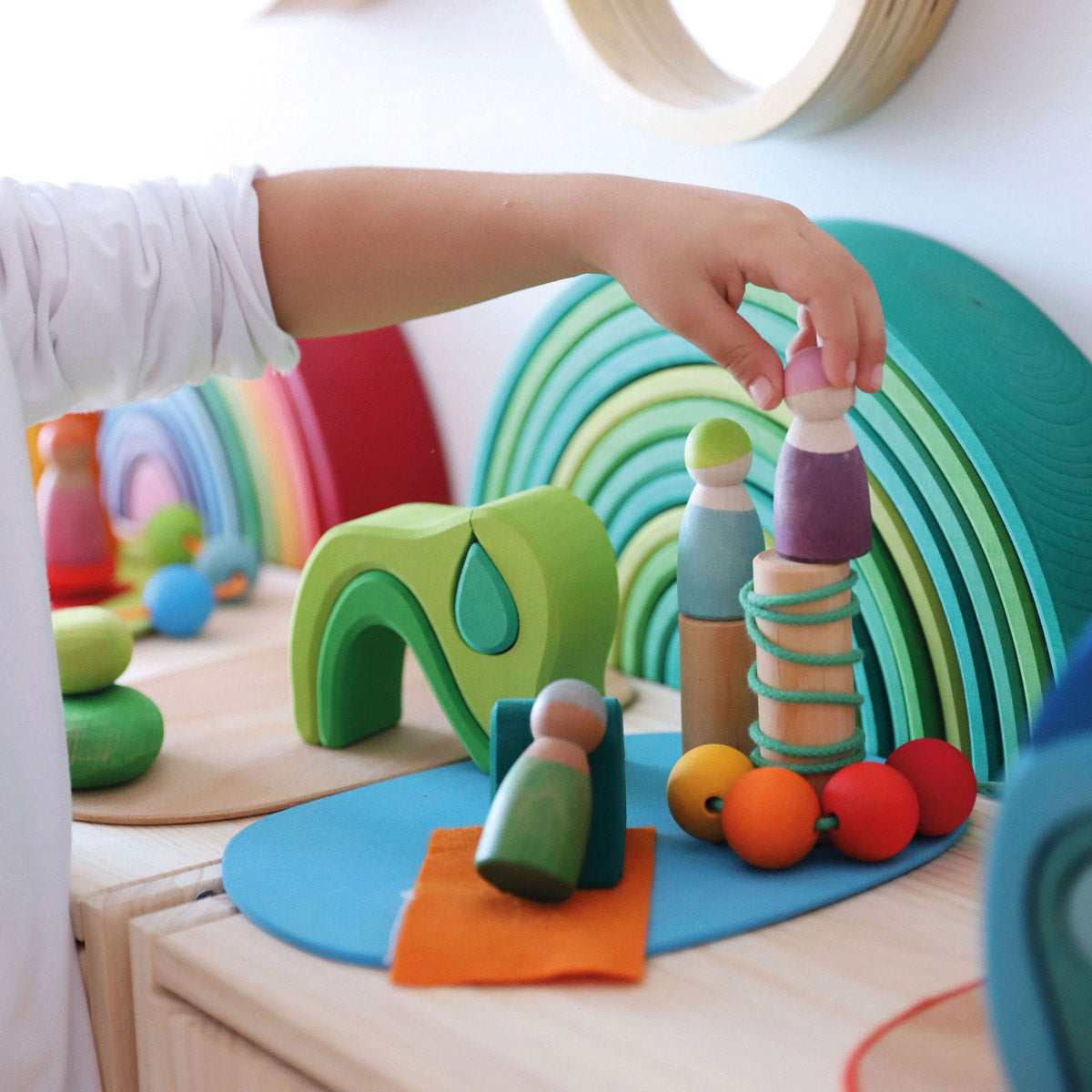 Girl smiling and playing with Grimm's Waldorf toy blocks on a wooden table