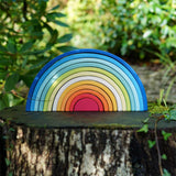 The Grimm's Gwawr Sunrise 12 Piece Rainbow placed on a tree stump outdoors.