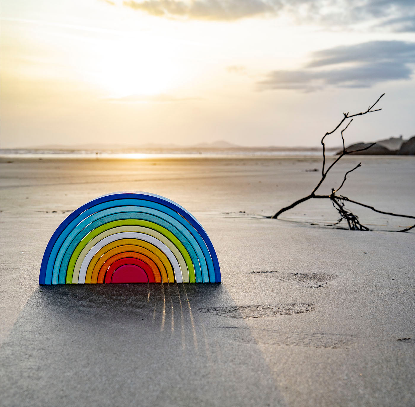 A Grimm's Gwawr Sunrise 12 Piece Rainbow placed on the sand on a beach. 