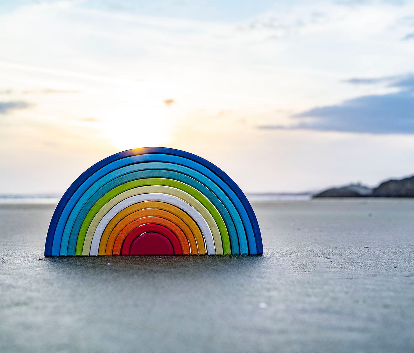 A Grimm's Gwawr Sunrise 12 Piece Rainbow placed on the sand on a beach. 