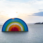 A Grimm's Gwawr Sunrise 12 Piece Rainbow placed on the sand on a beach. 