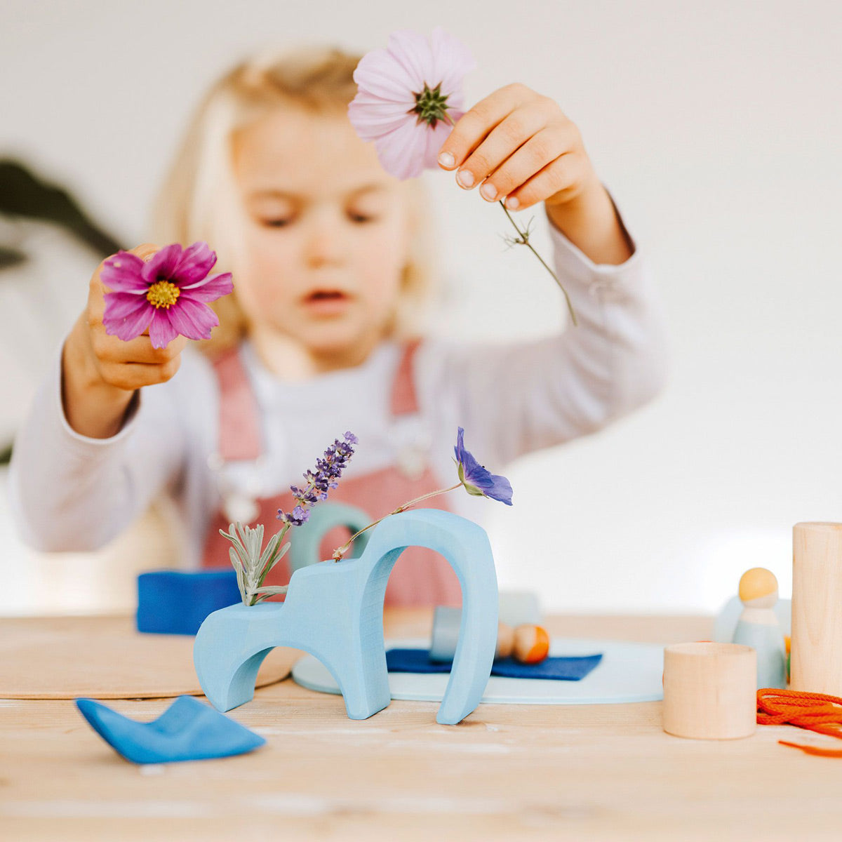 Close up of some hands playing with the Grimm's small world play toy set on a white table