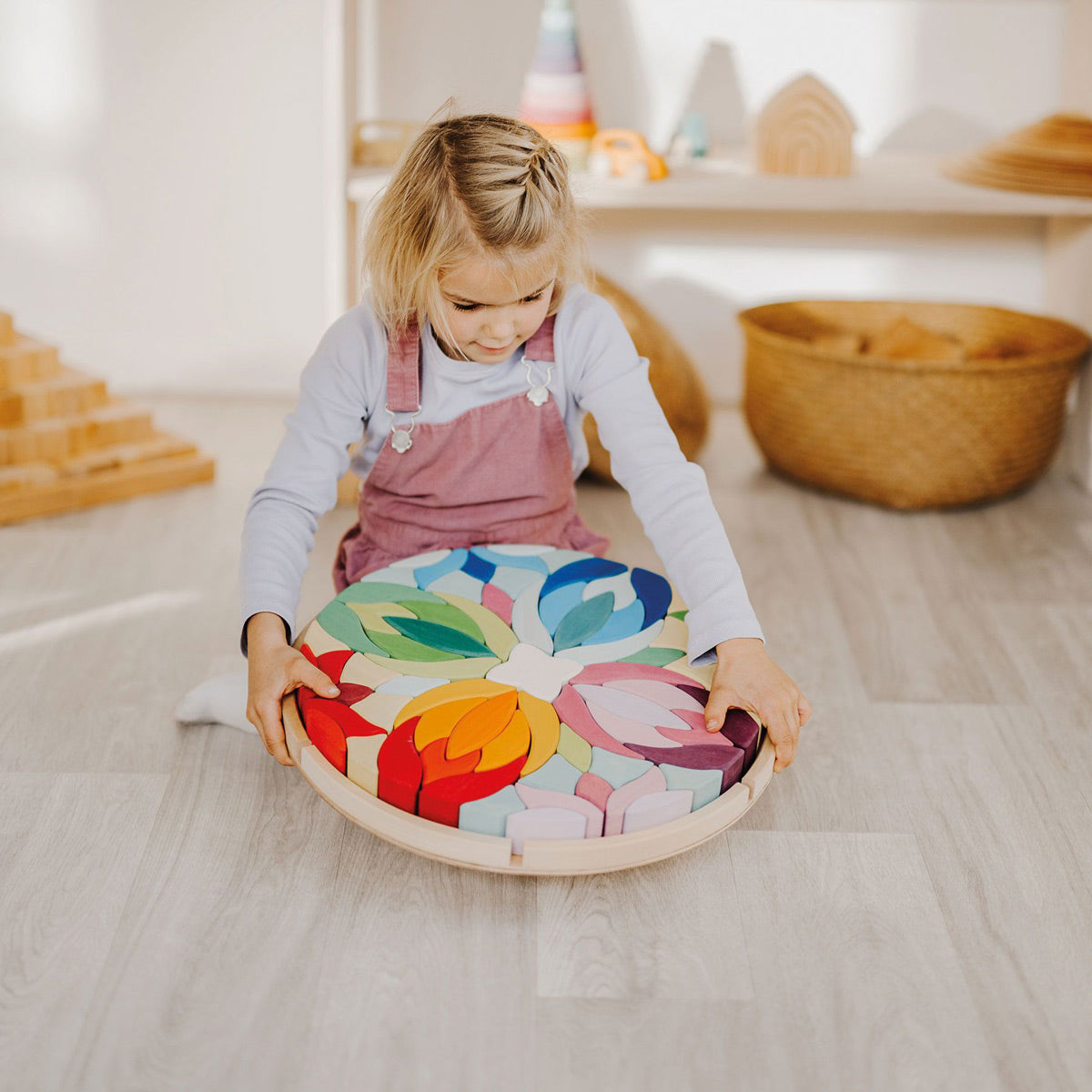 Young girl crouched on a wooden floor playing with the Grimm's wooden Lara toy blocks