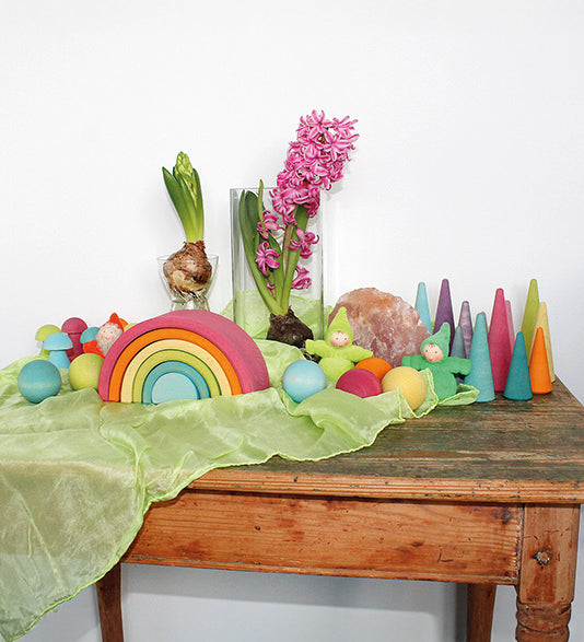 A Grimm's Medium Pastel Rainbow (6 Pieces) on a sideboard with other wooden Grimm's items including wooden balls, forest, mushrooms and gnomes. 