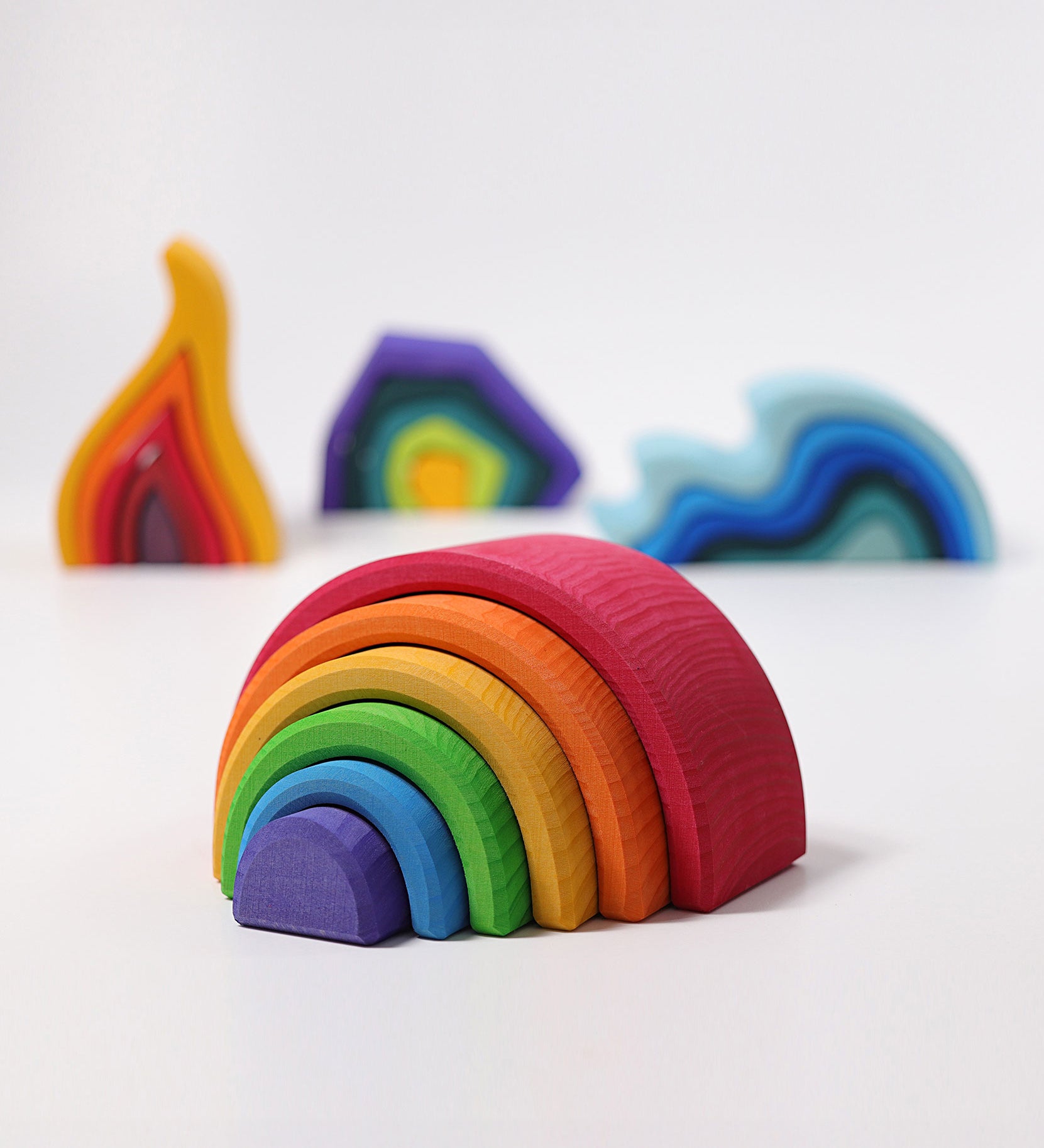 The Grimm's Medium Rainbow (6 Pieces) on a white surface with the other Grimm's element toys, fire, earth and water in the background. 