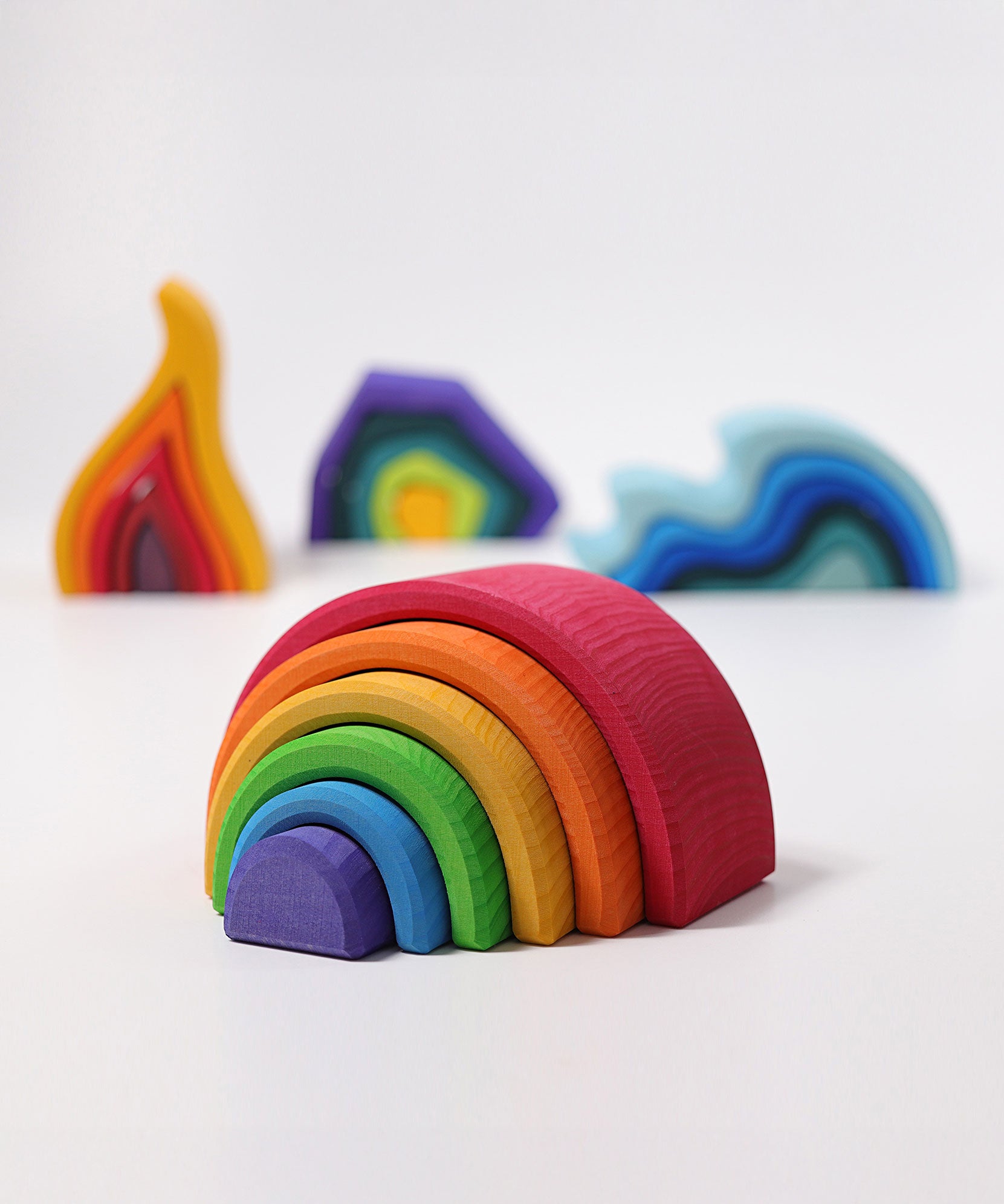 The Grimm's Medium Rainbow (6 Pieces) on a white surface with the other Grimm's element toys, fire, earth and water in the background. 