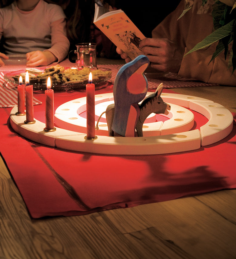 A Grimm's Natural Wooden Spiral set up on a table decorated with red Grimm's candles in brass holders and an Ostheimer donkey and Mary wooden figure. 