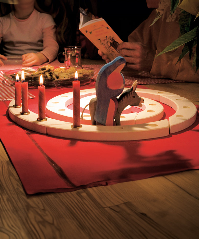 A Grimm's Natural Wooden Spiral set up on a table decorated with red Grimm's candles in brass holders and an Ostheimer donkey and Mary wooden figure. 