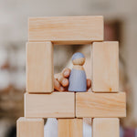 Close up of a child's hand holding a Grimm's Friend peg doll on a tower of Grimm's wooden toy blocks