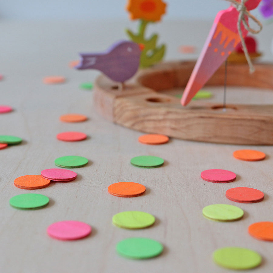 Grimm's Neon Celebration Confetti Dots. The dots surround a celebration ring on a wooden table.