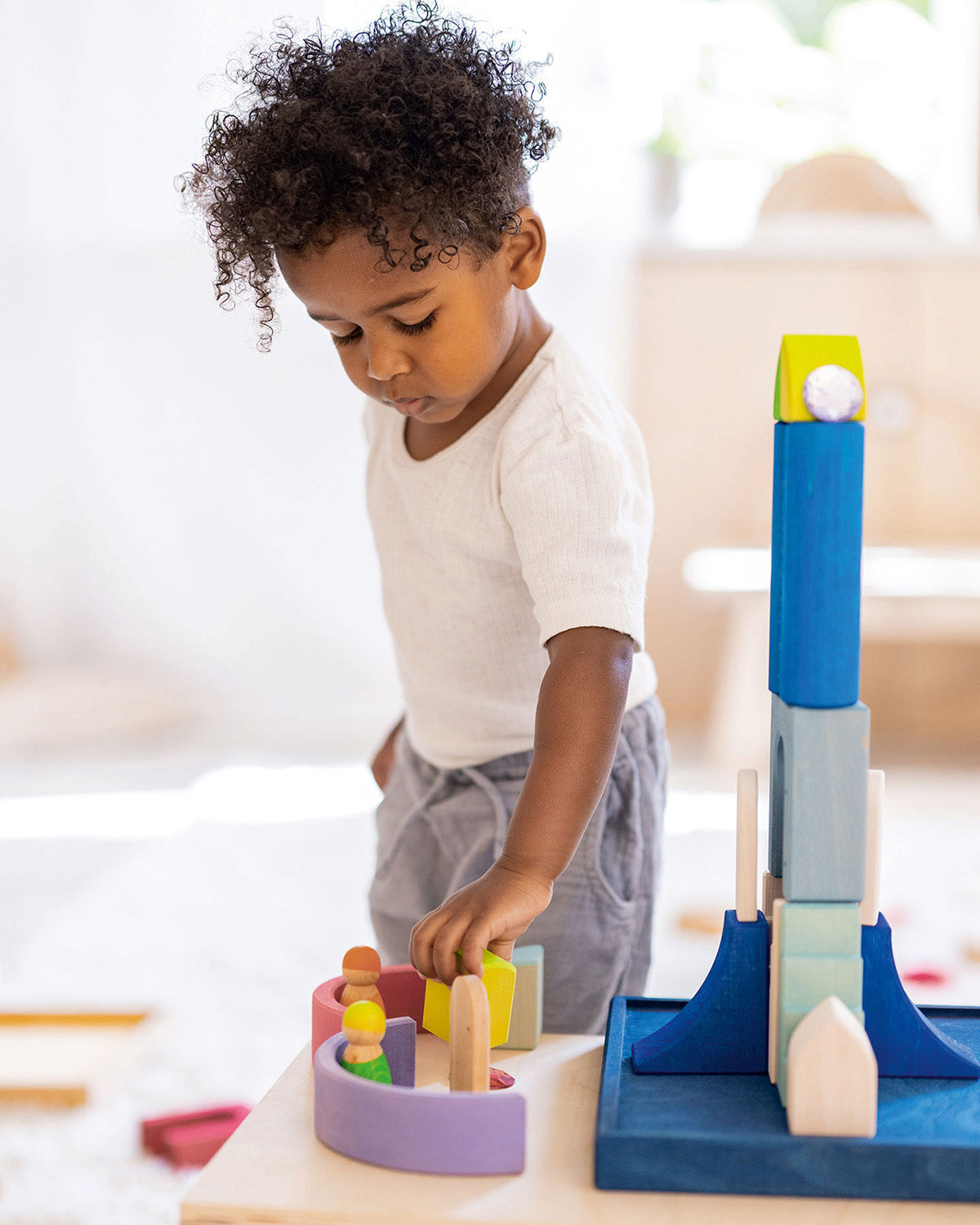 A child carefully balances a Grimms wooden figure on top of an arch