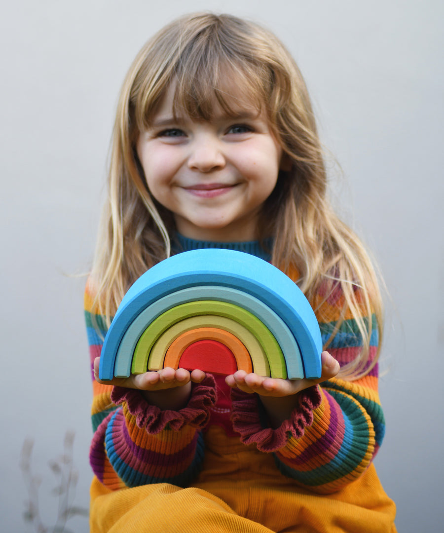 A child holding the Grimm's Babi Gwawr Sunrise 6 Piece Rainbow in their hands. 