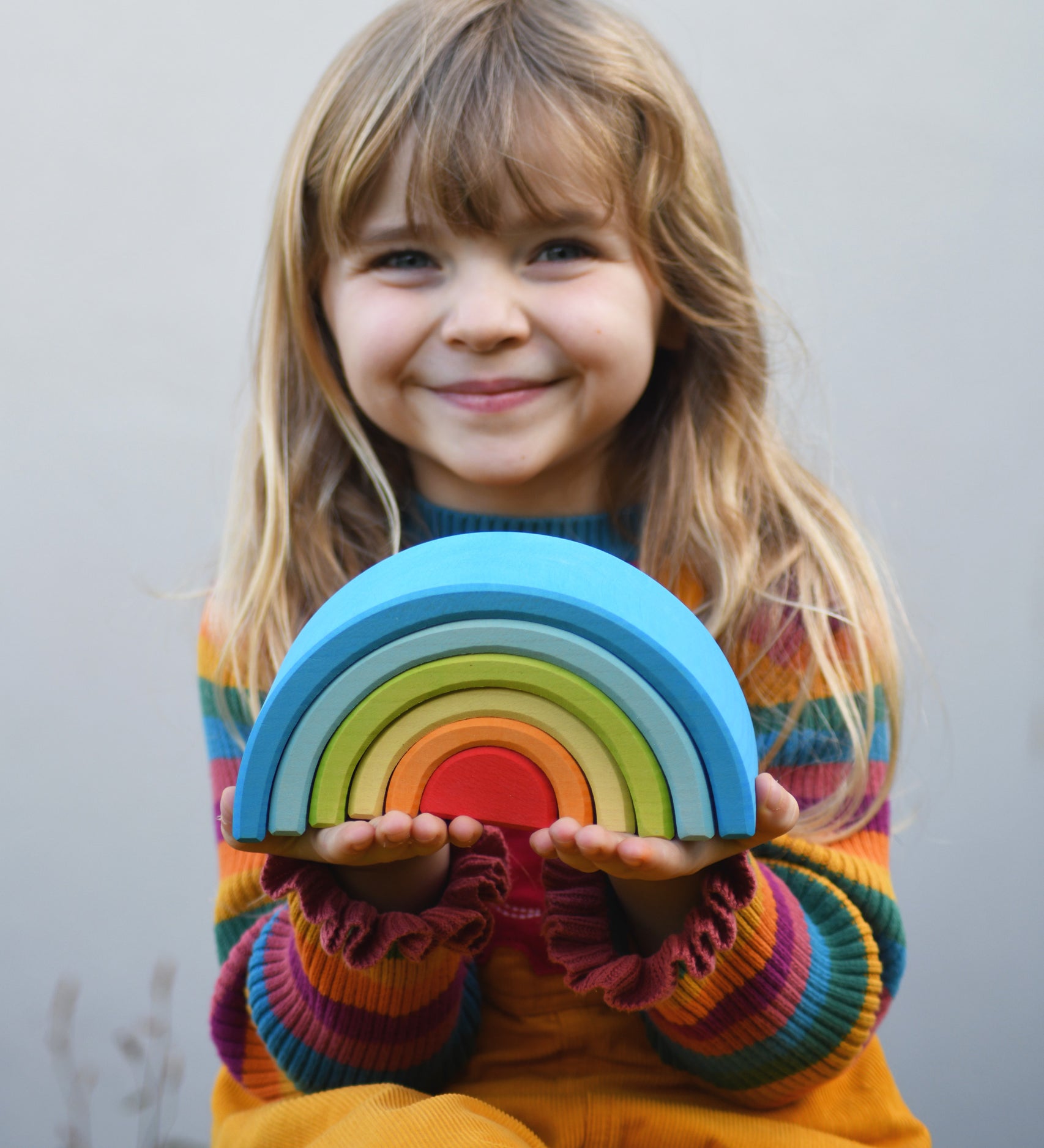 A child holding the Grimm's Babi Gwawr Sunrise 6 Piece Rainbow in their hands. 