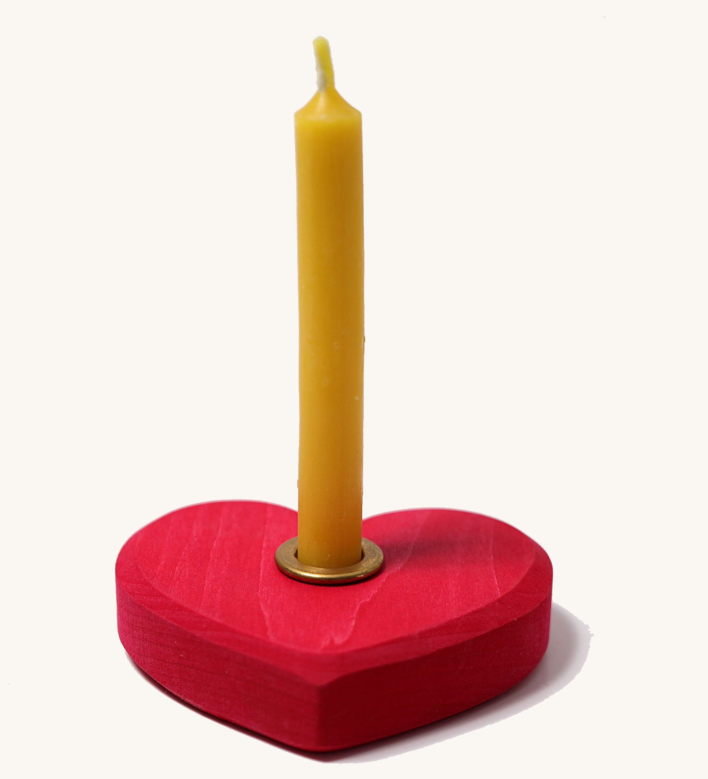 Grimm's Small Red Heart with a brass candle holder and candle on a plain background. 