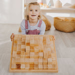 Young girl kneeling down holding up the Grimm's natural large stepped pyramid toy set