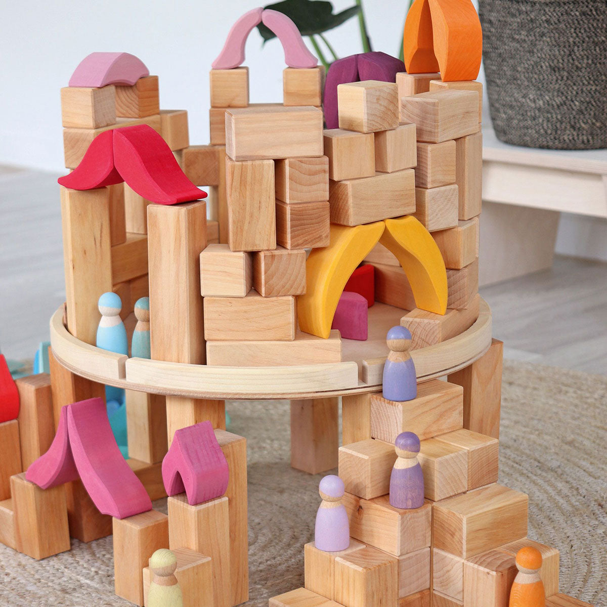 Grimm's wooden peg doll figures stood on top of a stack of Grimm's natural wooden toy blocks