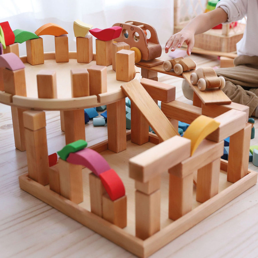 Grimm's large stepped pyramid Waldorf toy blocks stacked into a tower on a grey wooden floor