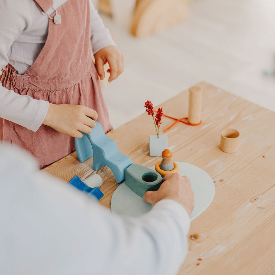 Young girl kneeling down and looking at a face made with some Grimm's plastic-free wooden toy blocks