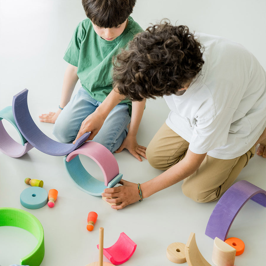 Grimm's 10-Piece Rainbow - Neon Pink. Two children play together with several sets of Grimm's Rainbows