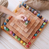 Close up of 2 children sat on the floor playing with some Grimm's wooden peg dolls and a natural Grimm's LSP