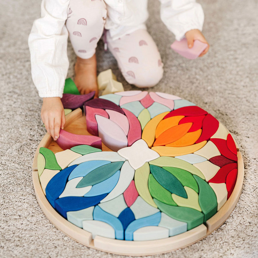 Close up of child's hand touching pieces of the Grimm's rainbow Lara mandala building blocks o a grey carpet