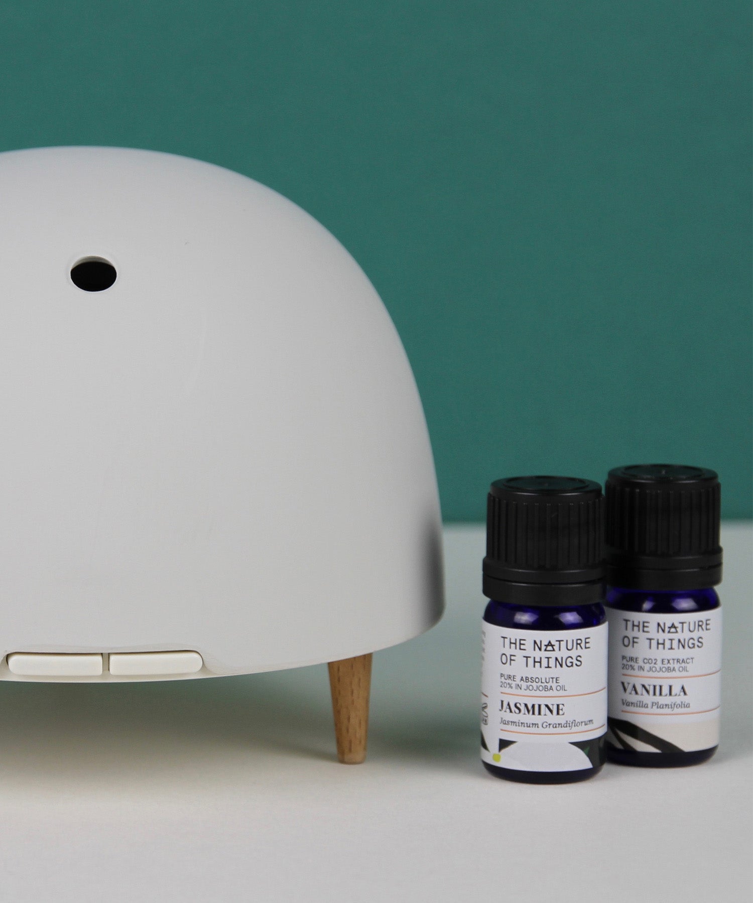 Maël Diffuser, a light grey dome plug-in essential oil diffuser with wooden feet, with two blue bottles of essential oils.