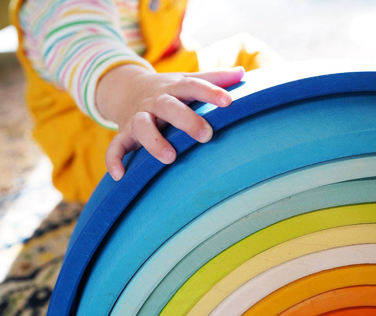 A close up of a child's hand on the Grimm's Gwawr Sunrise 12 Piece Rainbow.