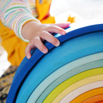 A close up of a child's hand on the Grimm's Gwawr Sunrise 12 Piece Rainbow.