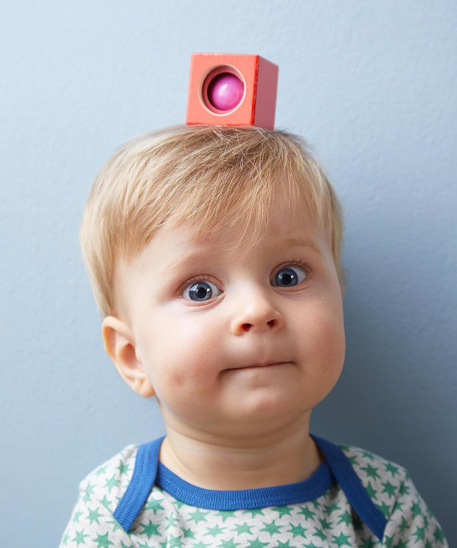 A red wooden block from the Haba blocks with sounds set on top of a child's head