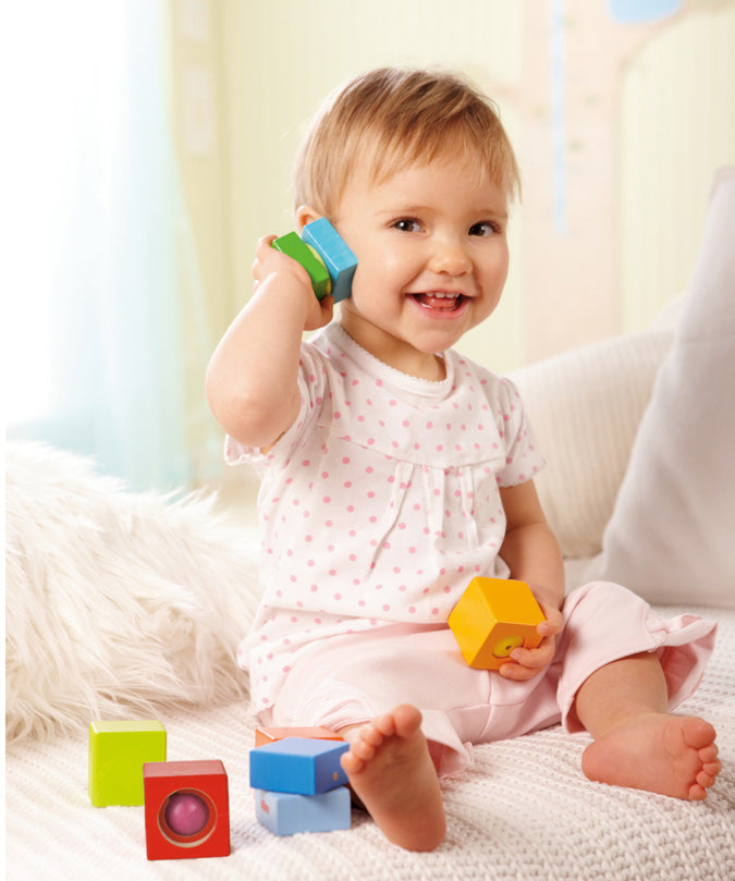 A child sitting with the blue and green wooden block from the Haba blocks with sounds set next to their ear