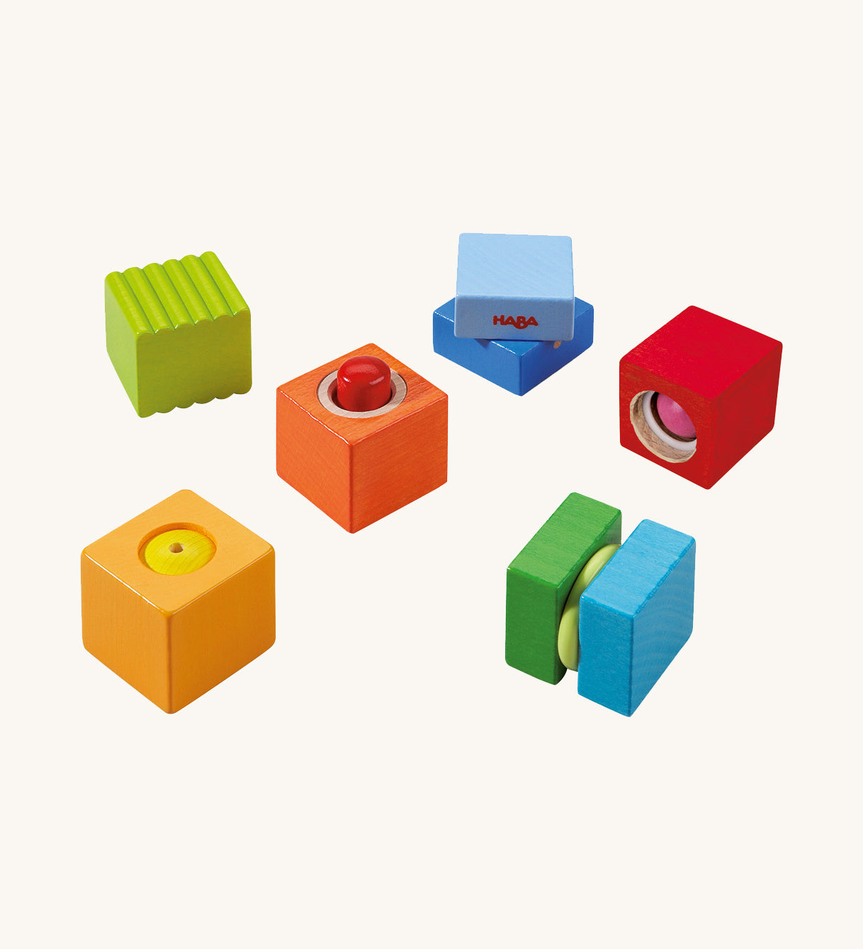 Green, orange, blue and red wooden cubes from the Haba blocks with sounds set on a cream background.