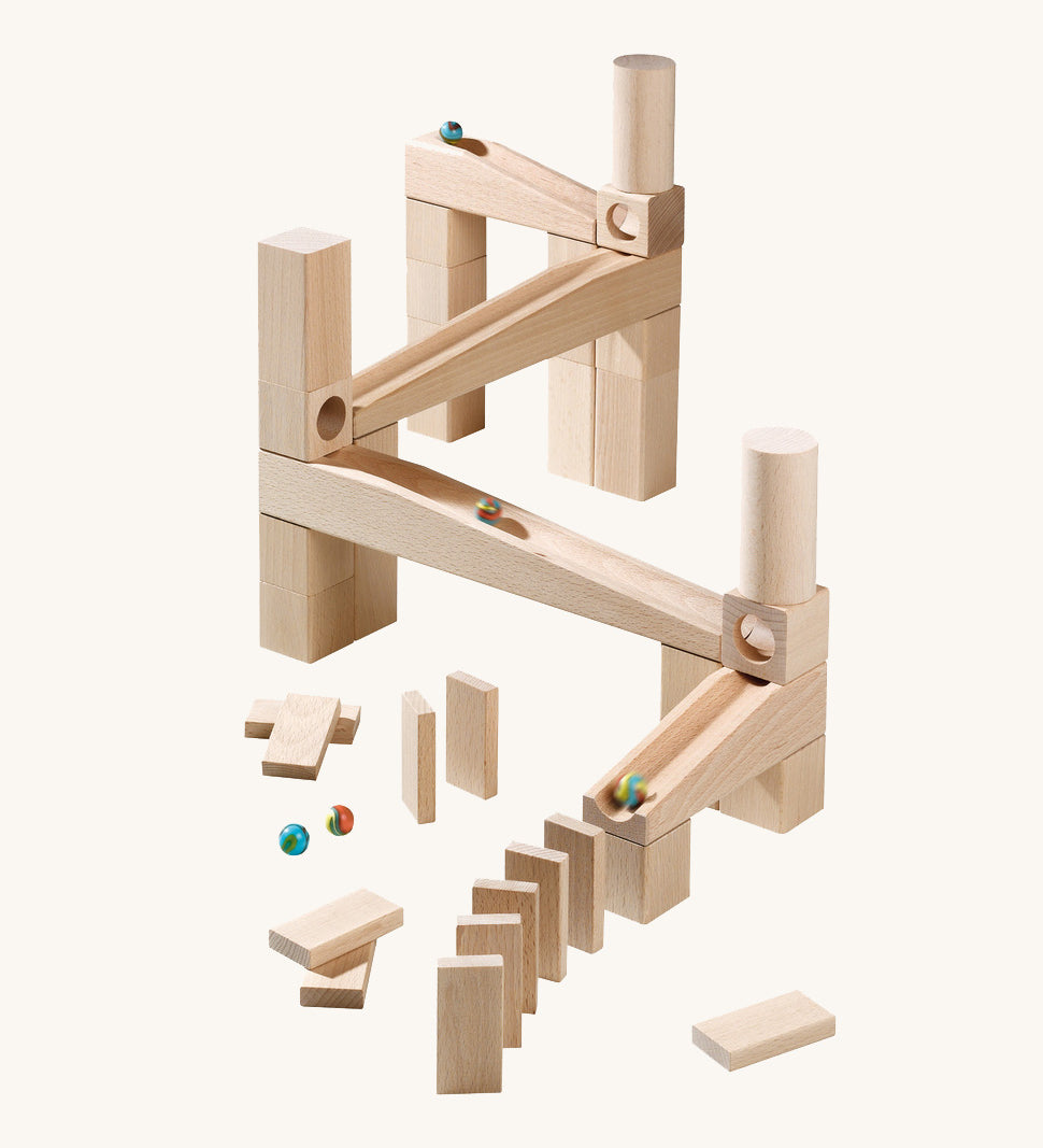 A marble run made from different natural wooden blocks from the Haba first playing blocks on a cream background.