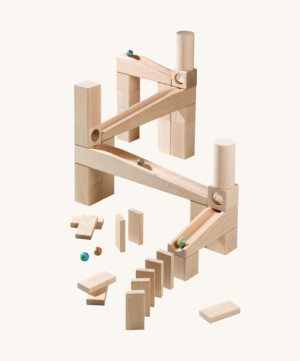 A marble run made from different natural wooden blocks from the Haba first playing blocks on a cream background.