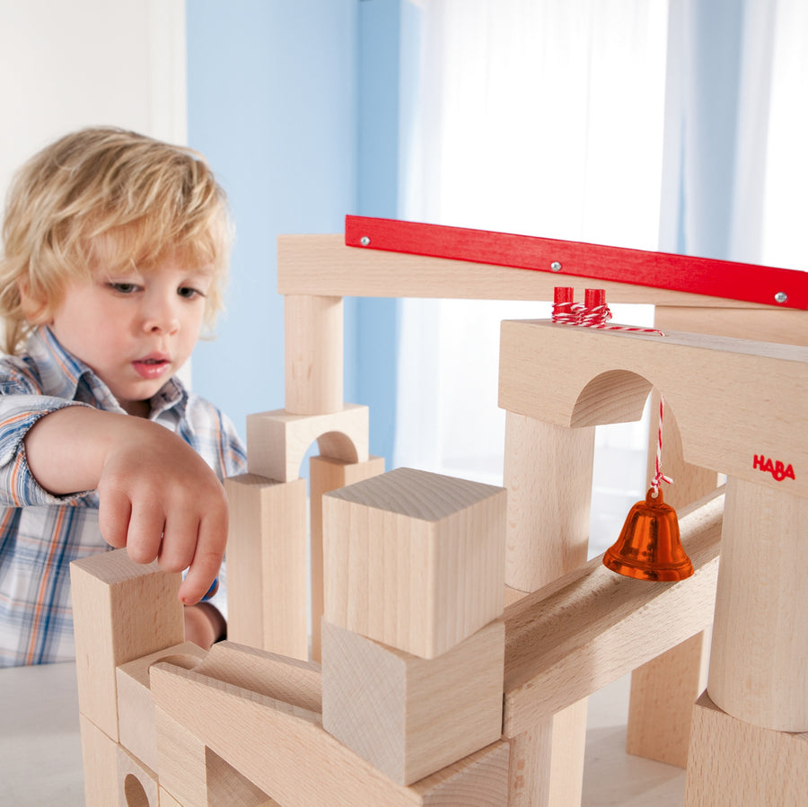 A child getting ready to roll blue marbles down the HABA Large Marble Ball Run. This image shows balanced natural wooden blocks creating a unique ball run